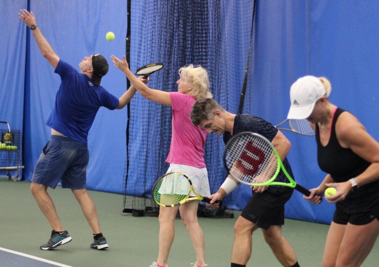 a group of adults practice their tennis serves during a tennis cardio class at a montrose athletic club