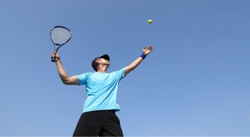 a gym member serves a tennis ball on an outdoor tennis court at a montrose gym